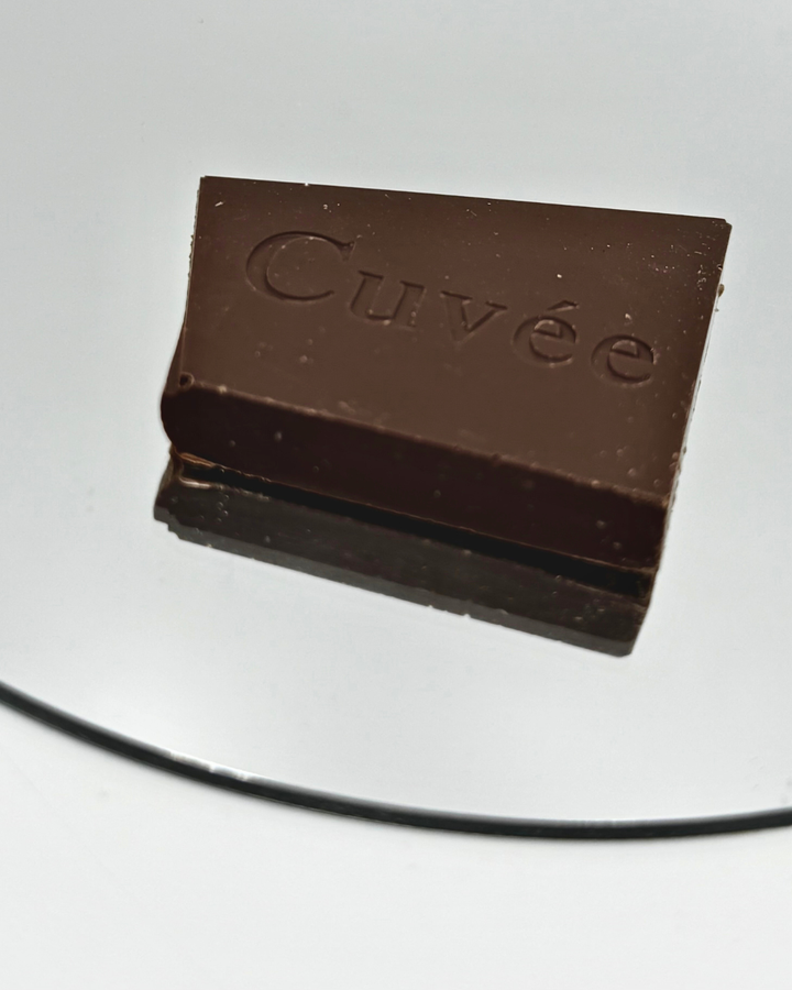 Close-up photo of a single piece of Cuvée dark chocolate on a reflective surface.
